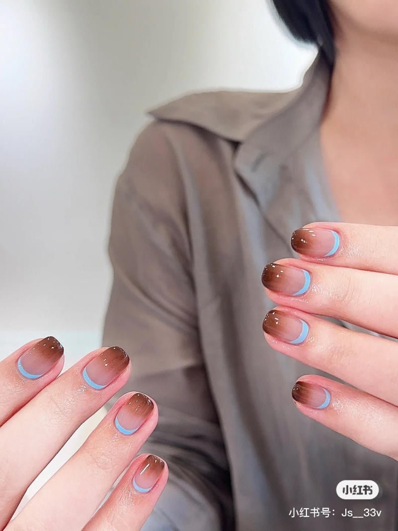 mau-nail-don-gian-cardina__144__758d50e341064ea193ae373943e8ef6f Bàn tay có móng tay được sơn màu nâu nhạt với đường viền xanh, người mặc áo màu nâu.