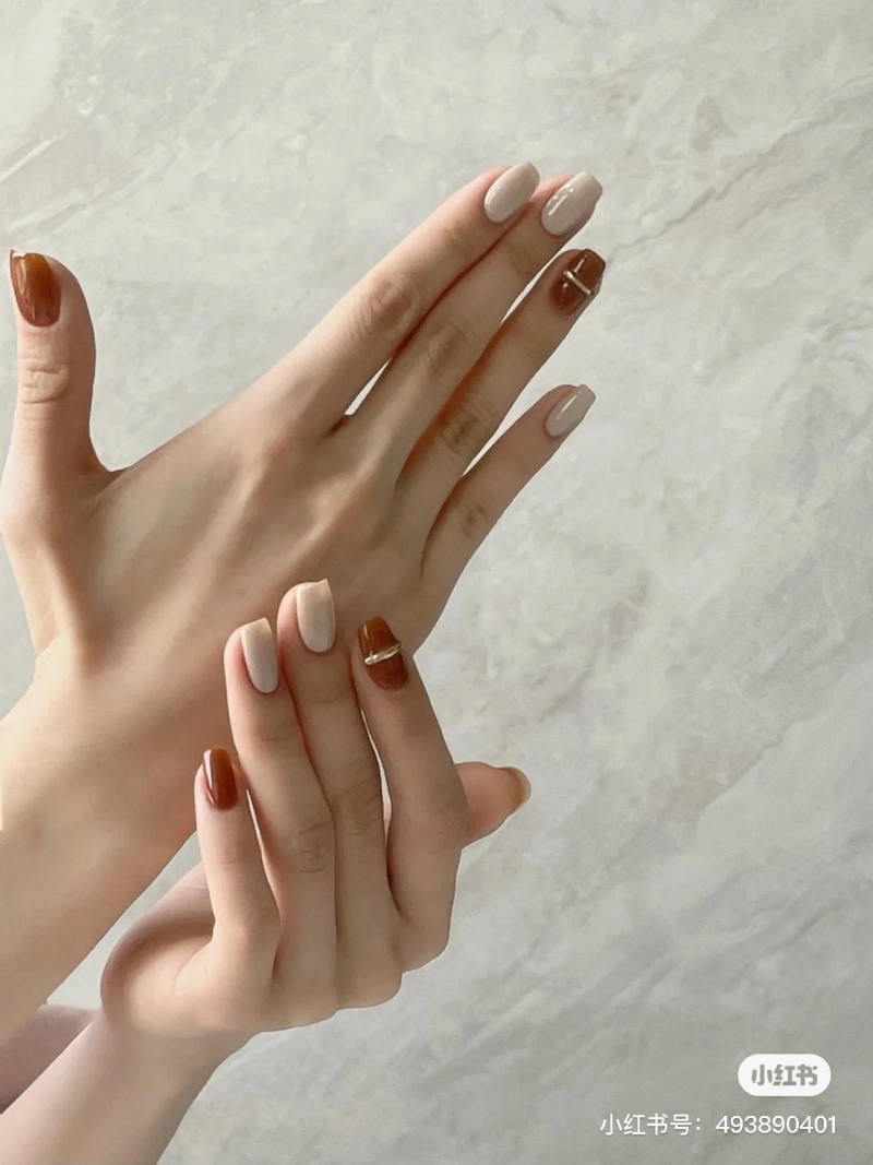 mau-nail-don-gian-cardina__145__e5382c5a31834e169528f9e8e46bf0ef Bàn tay với móng tay được sơn màu nâu và trắng, trên nền đá cẩm thạch.