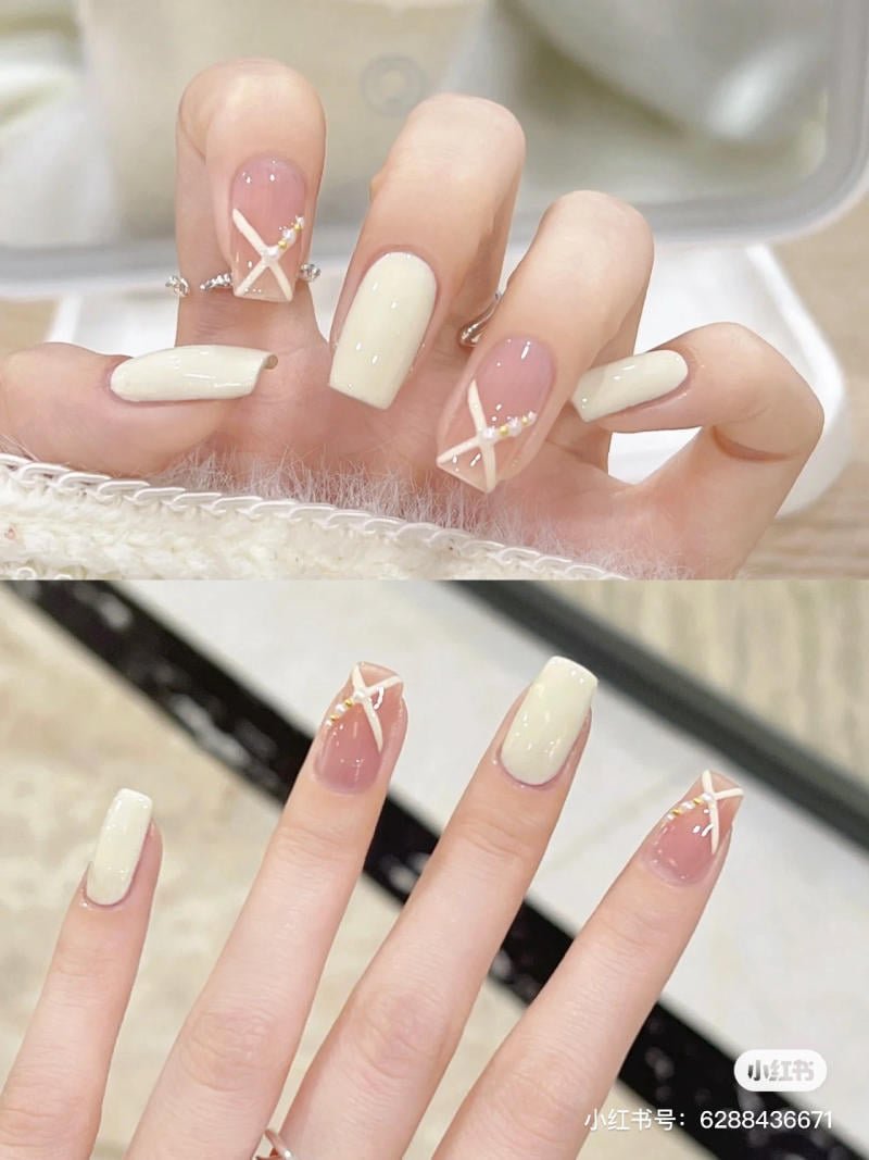 mau-nail-don-gian-cardina__74__09907e7b8db74a8ab83036d10555179e Bàn tay với móng tay được sơn màu trắng và hồng, có họa tiết đan chéo và đính đá trang trí.